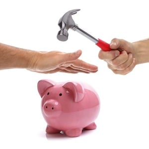 hand protecting piggy bank from hammer