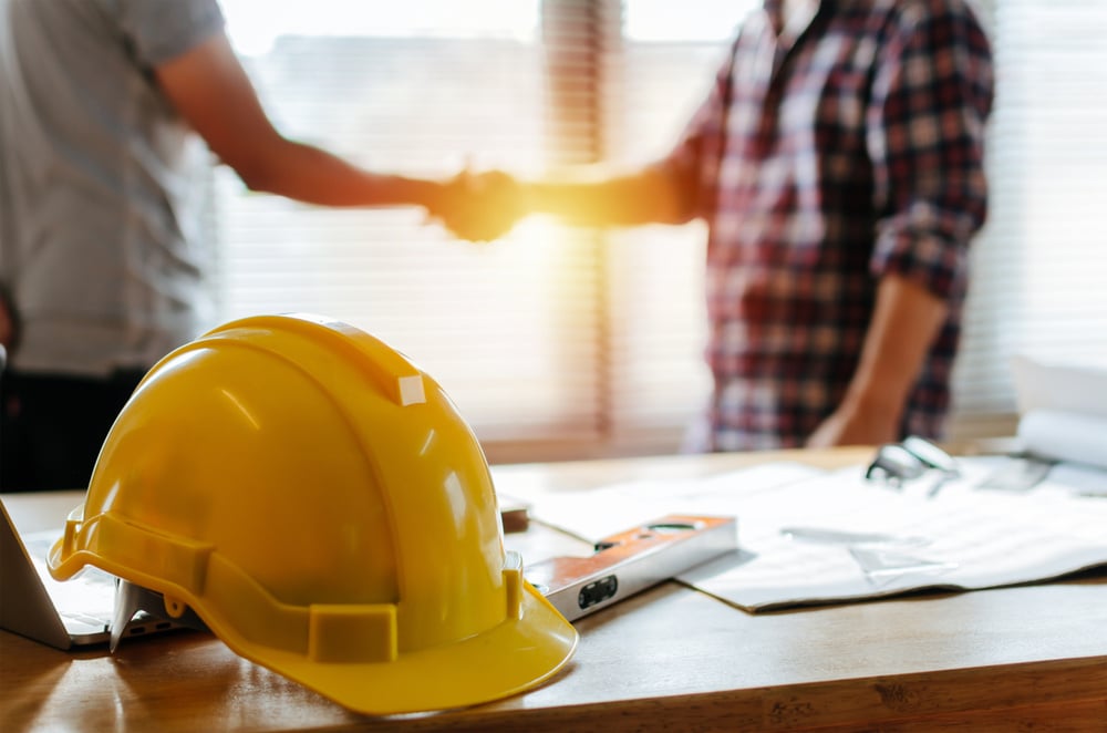 yellow contractor hat and two men shaking in the background